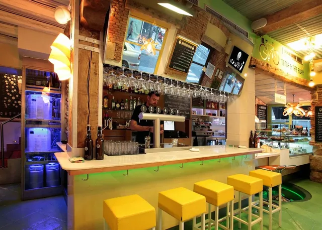 A lit bar with beer taps, yellow stools and an exposed brick wall