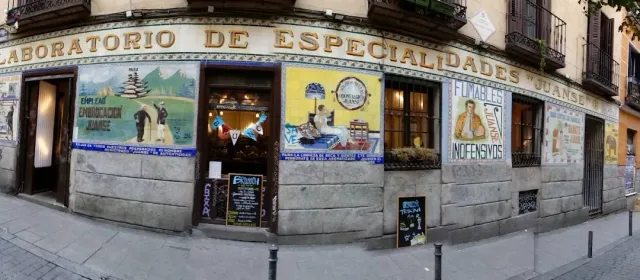 A corner shop front covered in painted tiles with lettering, and an open wooden door in the middle