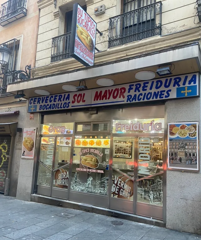 A bar facade with a large blue and red sign and pictures of dishes on the windows