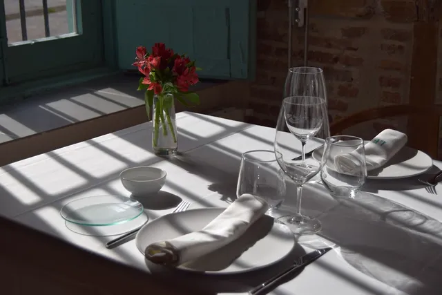 A set table in sunlight coming through a window, with a red bouquet and wine glasses