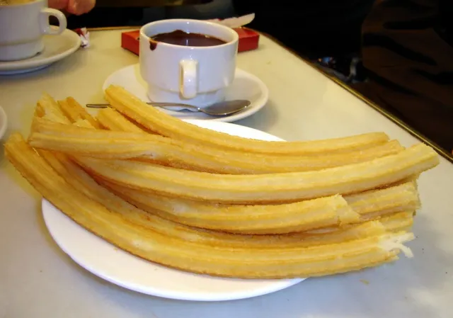 A plate of fried churros beside a cup of thick hot chocolate on a marble table