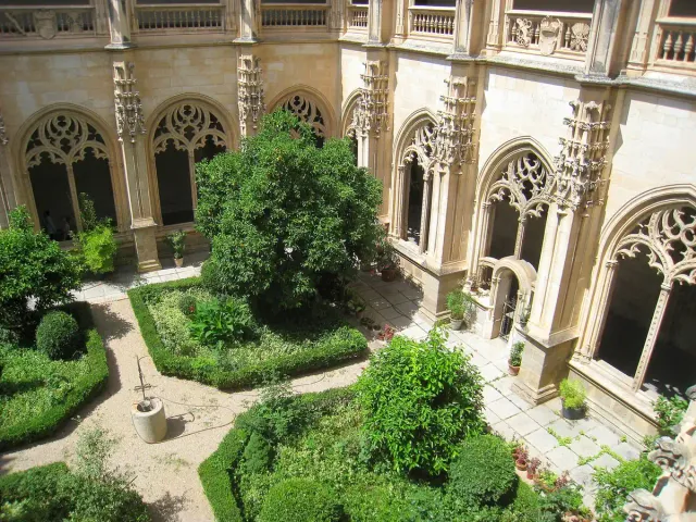 A Gothic monastery cloister with carved arches around a neat green garden