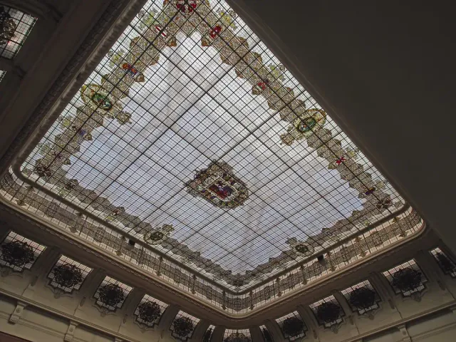 An exhibition hall with a large stained glass roof and galleries ringed by iron railings