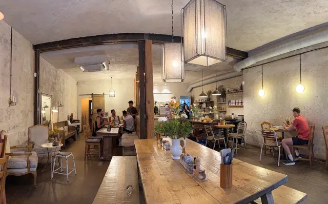 A hall with a long wooden table, hanging fabric lamps and diners by the counter