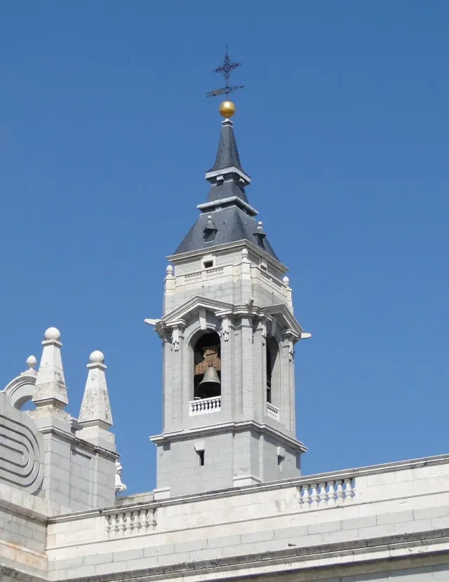 A white bell tower with a grey dome and rooftop statues against a blue sky