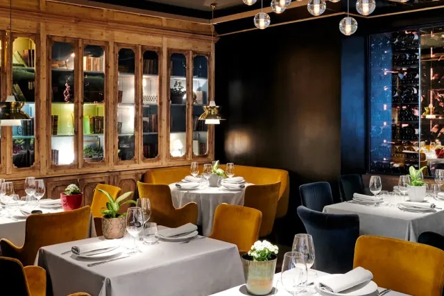 A restaurant interior with lit wooden cabinets, mustard and blue armchairs and set tables
