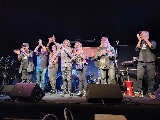A band taking a bow on a dark stage among speakers, drums and keyboards