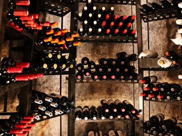 A wall of iron shelves packed with bottles of wine lying against a stone backdrop
