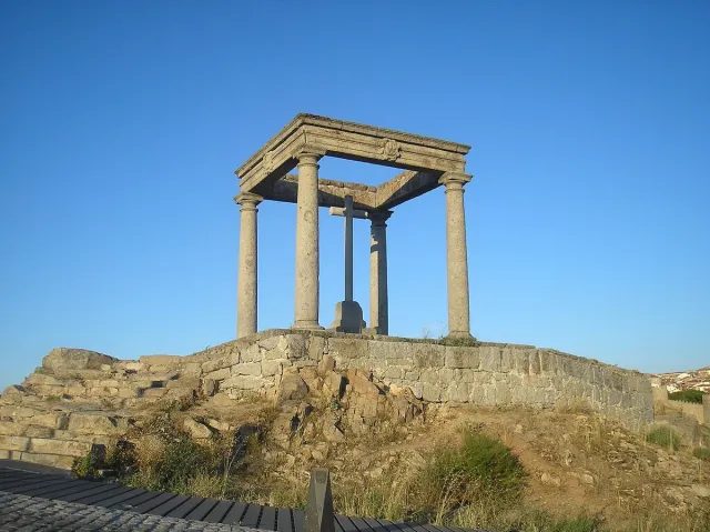 Four stone columns carrying a square cornice and a cross on a rocky hill in the evening