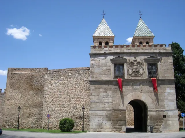 A stone city gate with two green tiled spires and a carved coat of arms beside an ancient wall