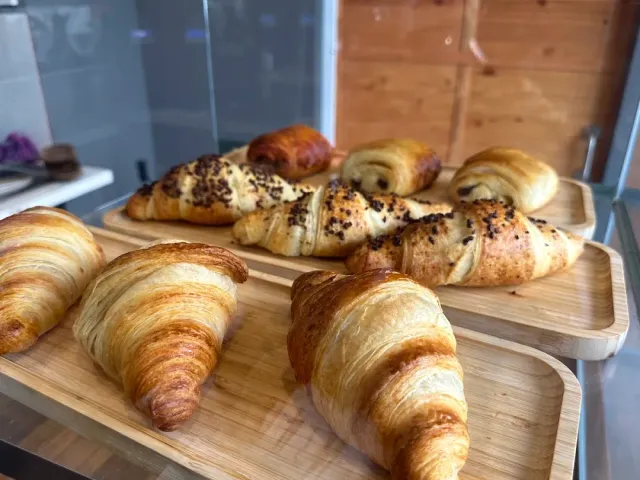 Croissants and chocolate pastries arranged on wooden trays inside a display case