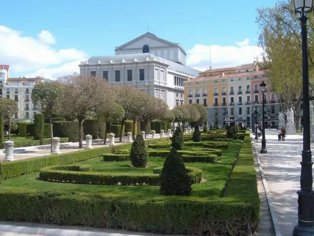Neatly clipped formal gardens in front of a wide white theatre building