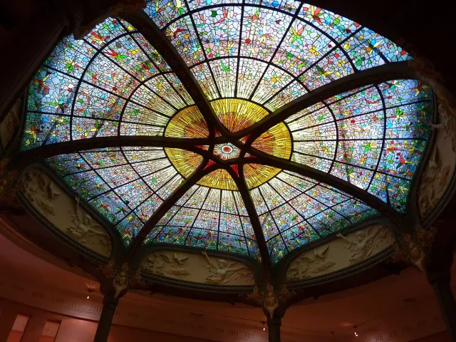 A colourful stained glass dome seen from inside, with a floral pattern around a golden centre
