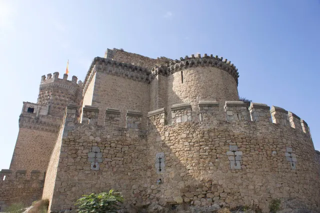 A stone castle with round towers and a crenellated wall against a cloudy sky