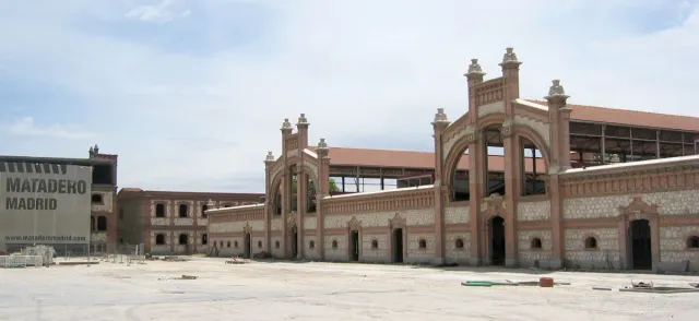 A complex of low brick buildings with arched gateways and a paved forecourt