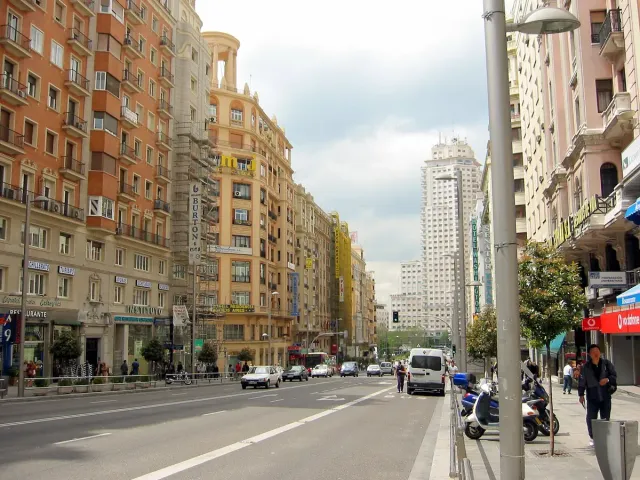 A wide avenue lined with tall stone buildings, moving traffic and pedestrians