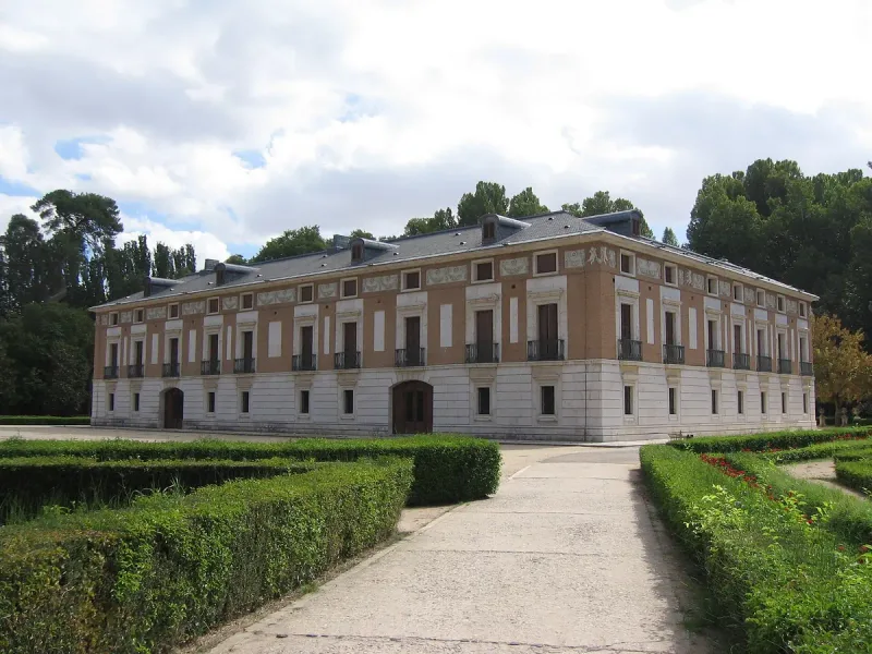 A small two storey palace of brick and white stone with a path and clipped hedges in front of it