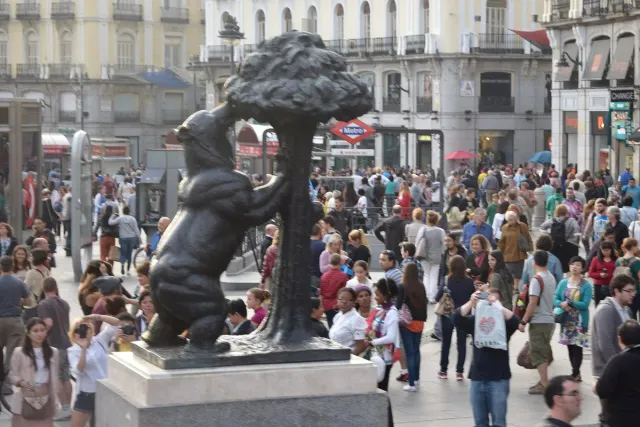 A bronze statue of a bear reaching up into a tree, with a crowded square behind