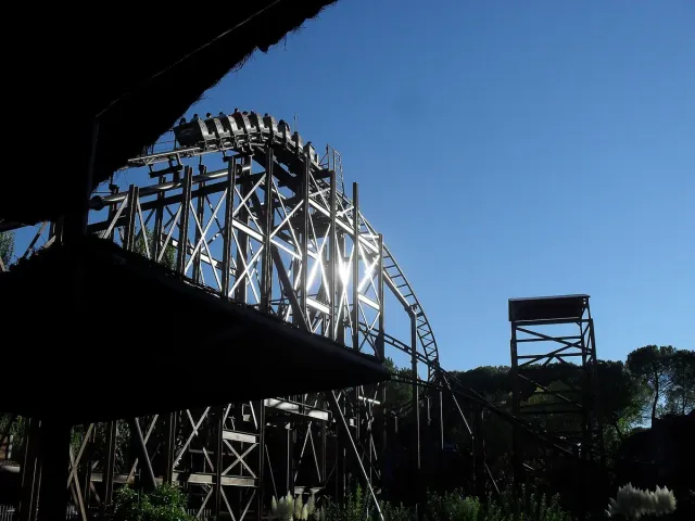 A steel roller coaster structure curving above trees against a bright sky