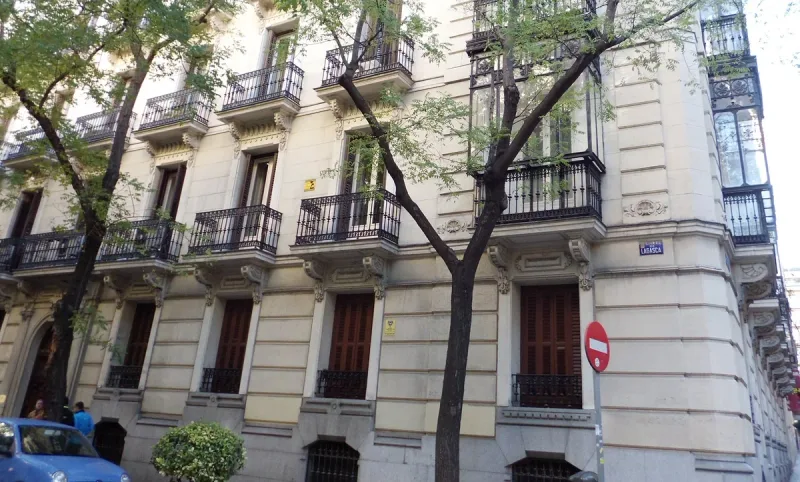 A pale stone building front with wrought iron balconies and a blue street plaque reading Lagasca