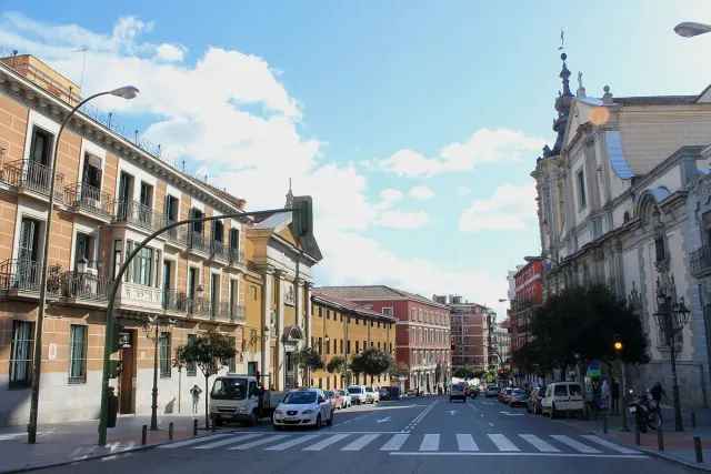 A broad street with a pale Baroque building at its end, cars and trees on both sides