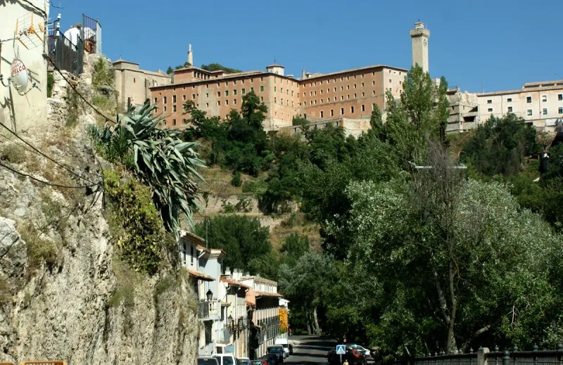 A rock slope with the old town of Cuenca above it and a pale stone tower at the end of the ridge