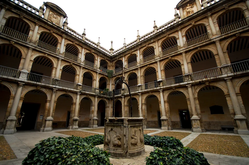 An inner courtyard with two tiers of stone arches and a carved wellhead between clipped hedges