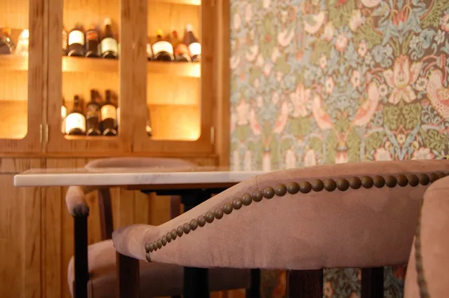 Pink velvet armchairs by a marble table, a lit wine cabinet and floral wallpaper