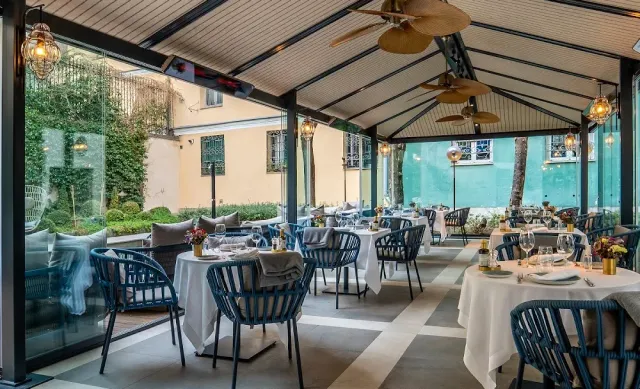 A covered patio with ceiling fans, blue rattan chairs and tables in white cloths