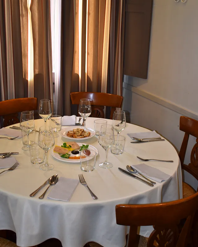 A round table set with a white cloth, wine glasses and a small starter plate in the middle