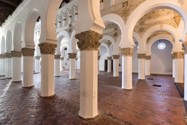 A hall of white pillars with decorated horseshoe arches and a terracotta tiled floor