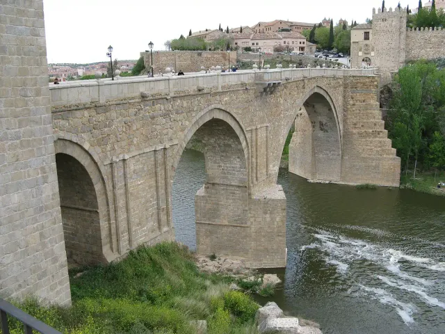 A medieval stone bridge with wide arches over a river, with a gate tower at one end