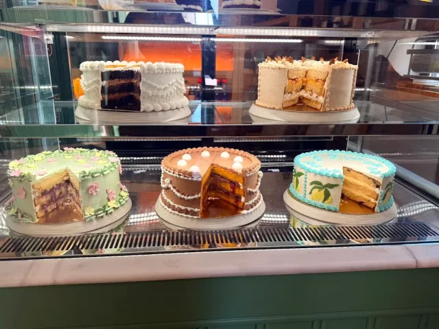 Five decorated layer cakes with slices cut out inside a lit two level display case