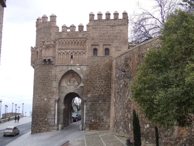 A brick and stone city gate with a double horseshoe arch and a round carved relief above it
