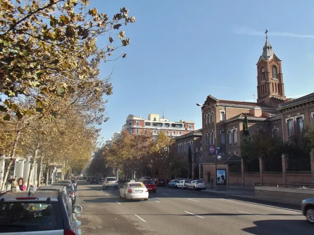 A city avenue lined with trees in autumn colours and a brick bell tower at its end