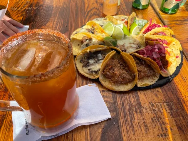 A platter of tacos with different fillings and lime slices, beside a glass of beer on a wooden table