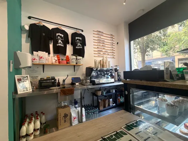 A counter corner with shirts hanging, a menu on the wall and an espresso machine