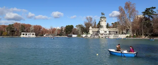 A wide lake with rowing boats and a colonnade topped by an equestrian statue on its bank