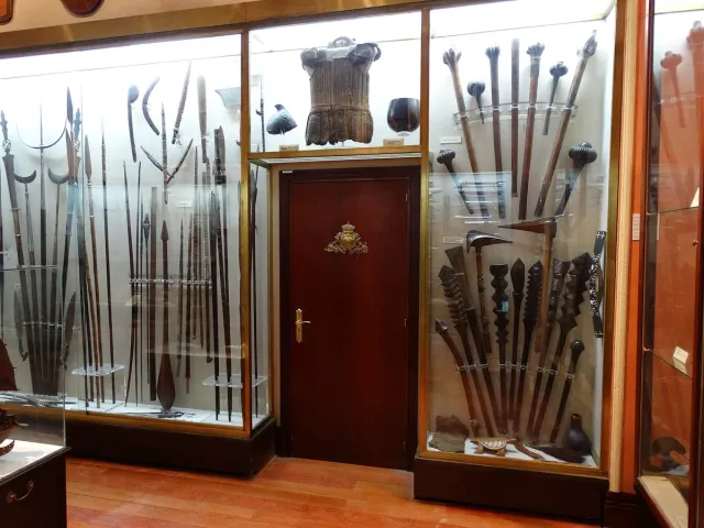 An exhibition hall with wood and glass cases holding spears, clubs and antique weapons