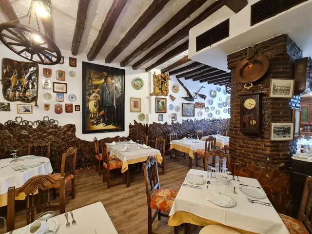 A rustic dining room with wooden beams, a wagon wheel chandelier and walls covered in pictures and plates