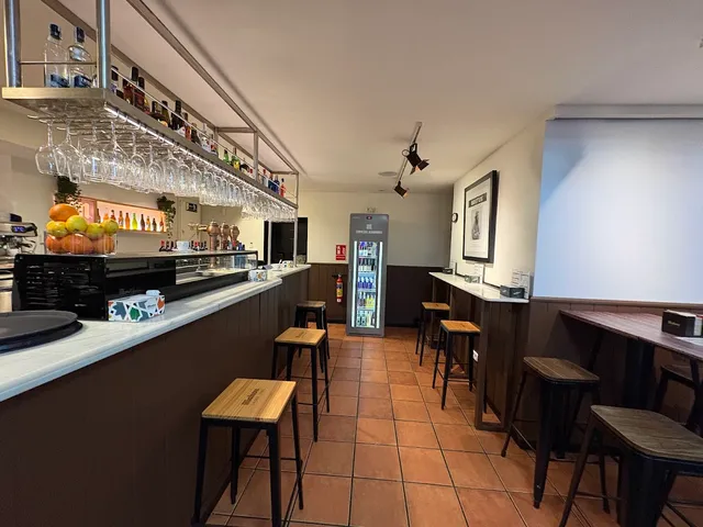 A narrow bar with a marble counter, hanging glasses and wooden stools along the wall