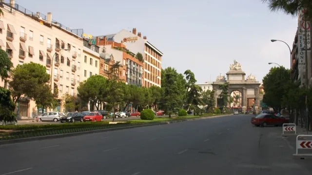 A broad tree lined street with a monumental stone gate and central arch at its end