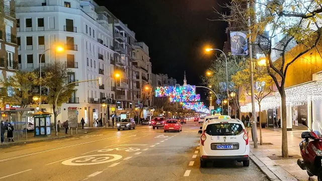 A boulevard at night with cars, a parked taxi and colorful light decorations above the road