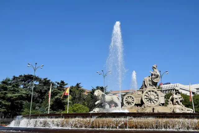 A fountain with a marble statue of a goddess on a lion drawn chariot and a tall jet of water behind