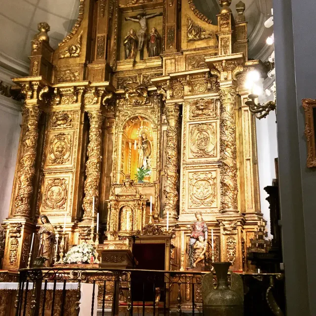 A gilded carved wooden altarpiece rising the full height of the wall, with twisted columns and a painting at its centre