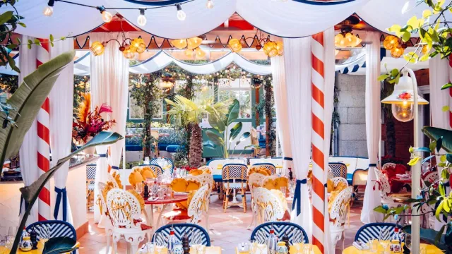 A decorated room with white drapes, string lights, striped columns and wicker chairs
