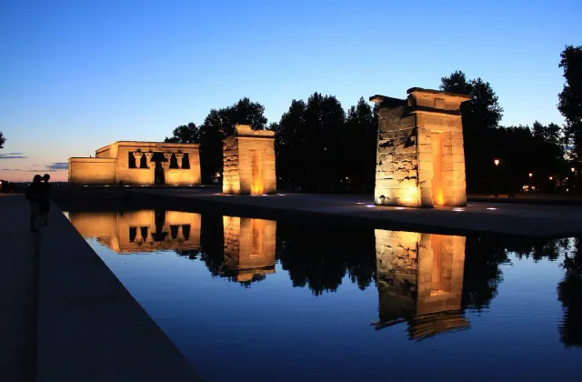 An Egyptian stone temple with arched gateways reflected in the pool before it in evening light