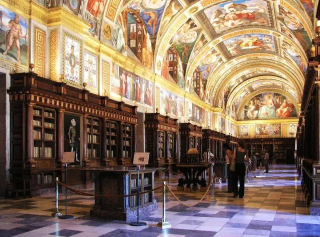 A long library hall with a vaulted ceiling painted in frescoes and wooden bookcases along the walls