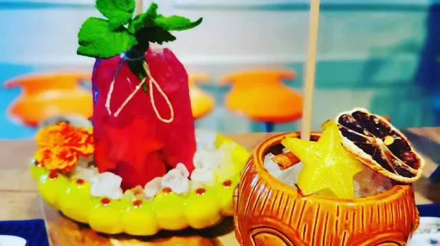 A red cocktail garnished with mint beside a tiki mug with a star fruit slice and a dried citrus slice