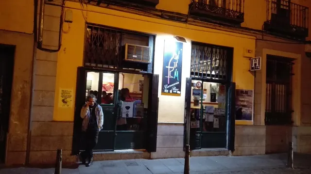 The yellow facade of a bar at night with a lit sign and doors open to the street